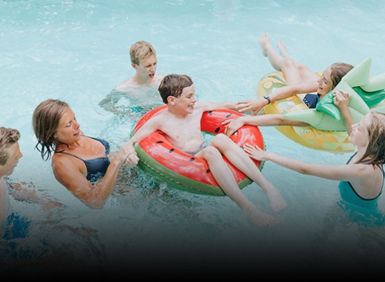 family in the pool with two kids in watermelon and pineapple inner tubes