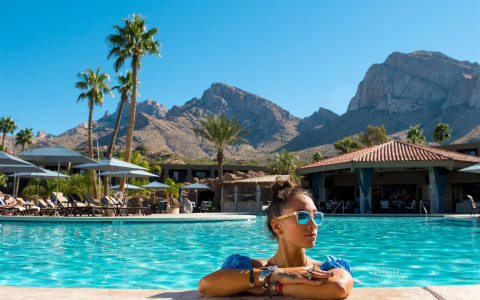 girl sitting in pool with sunglasses on and mountains in background