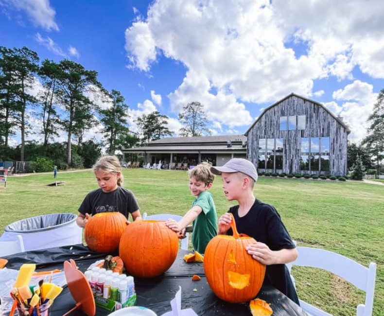 three kids outside sitting a table carving pumpkins