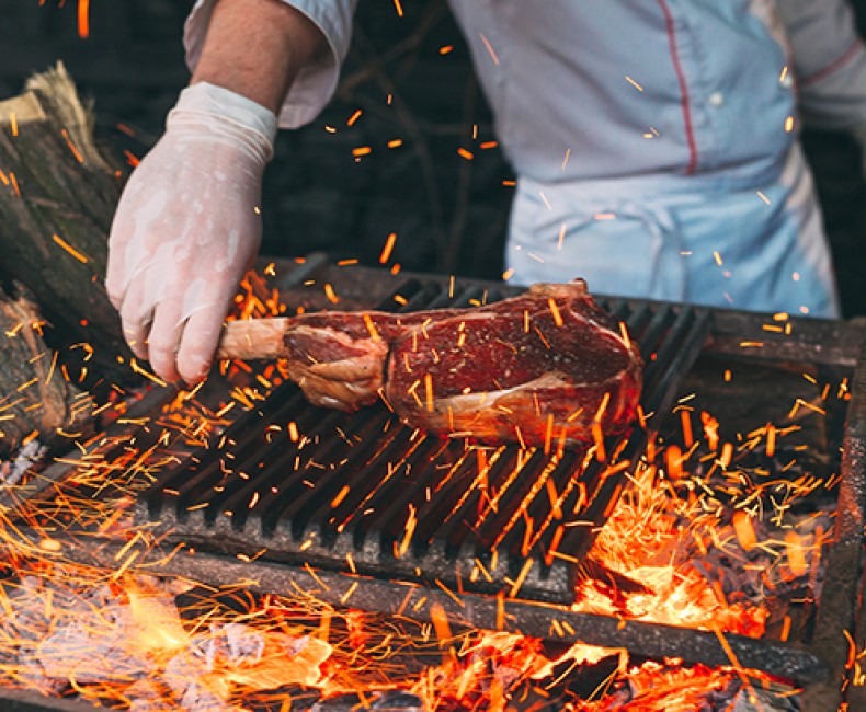 man preparing meat on an open flame grill