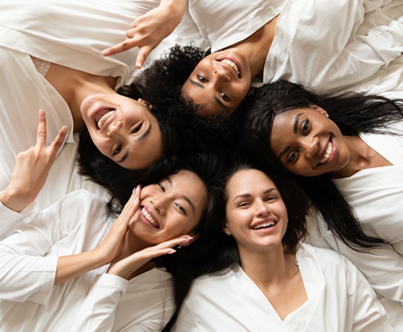 4 women laying on a bed laughing