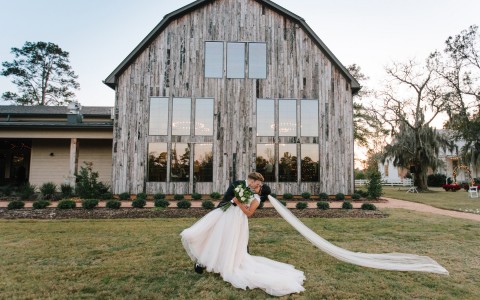 bride with long train standing in front of the barn 