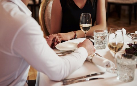 close up of a man holding a woman's hand while sitting at a table with glasses of white wine