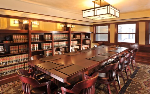 a large meeting room with a long rectangle table and a wall of books behind it