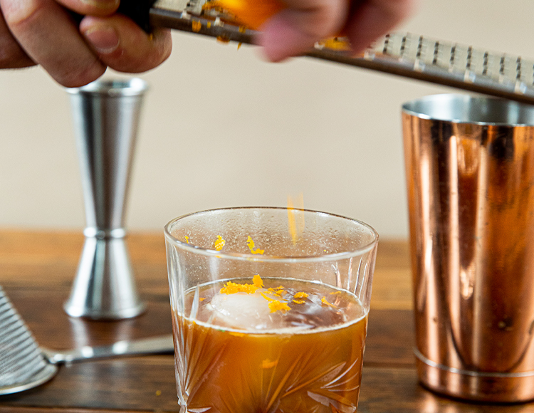 a bartender garnishing a drink with grated orange rind
