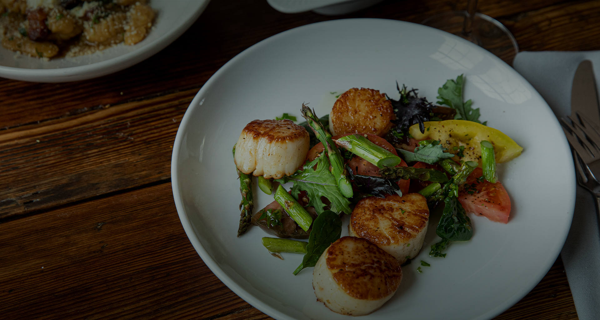 close up of a seared scallop entree served with fresh mixed greens and tomatoes
