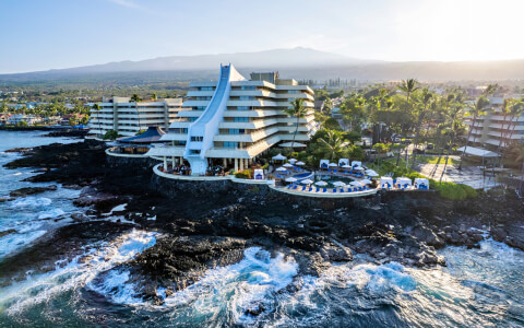 aerial view of royal kona resort with ocean waves crashing upon the rocky shore