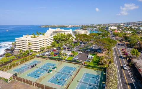 aerial view of several resort tennis courts with ocean backdrop