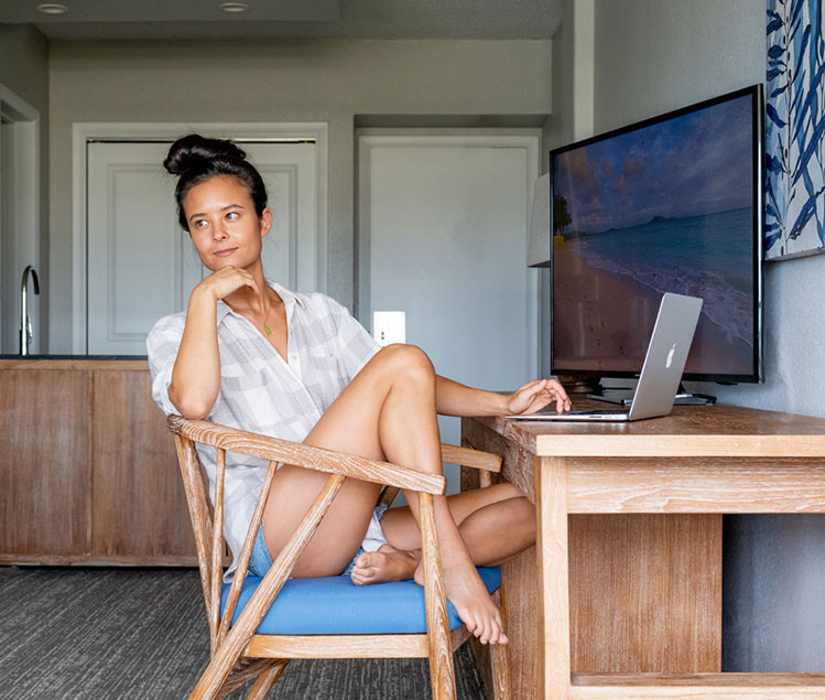 A woman sitting on a desk chair with a computer and a tv in front of her