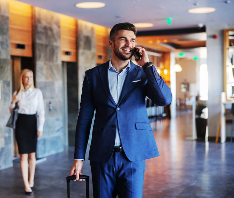 Dark haired man with luggage walking through lobby with blonde haired woman behind him