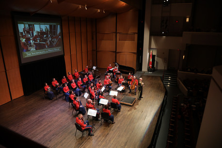 Small Orchestra performing in front of a screen in red uniforms
