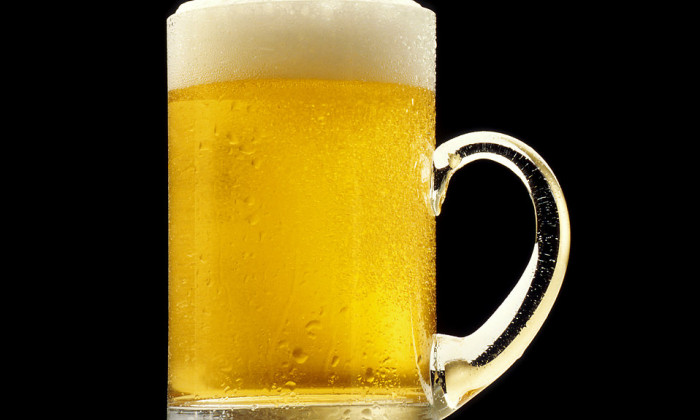 Glass mug of beer with foam head and a black backgroung