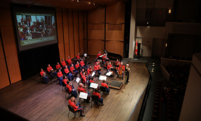 Small Orchestra performing in front of a screen in red uniforms
