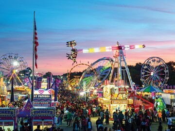 Crowds of people at the Arkansas Fairgrounds with ferris wheels and other rides visible