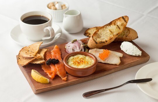 Assortment of breakfast items on a wood plate and a cup of coffee