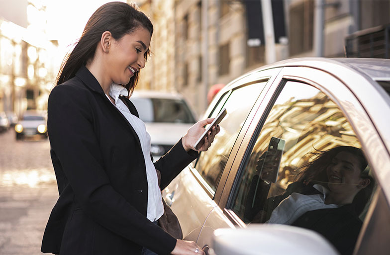 a business woman answering an email on her phone standing next to her car