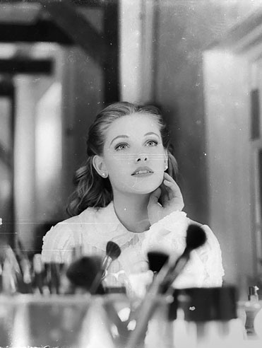 Black and white image of young woman looking into mirror with makeup brushes on vanity