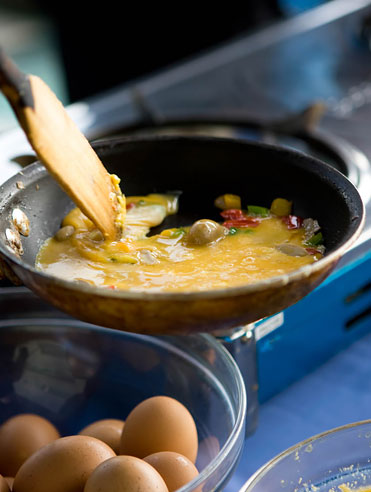 Bowl full of eggs next to pan cooking omelette