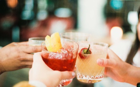 close up of four hands holding cocktails and toasting