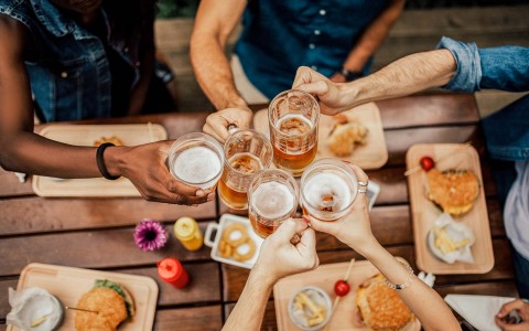 A group of friends eating hamburger and toasting with beer glasses