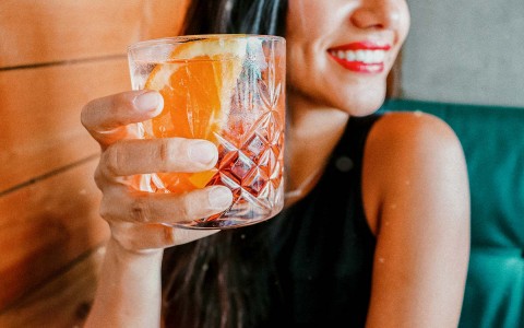 close up of a woman smiling and holding a red cocktail with orange