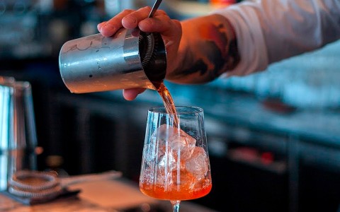 bartender pouring a red cocktail into a glass