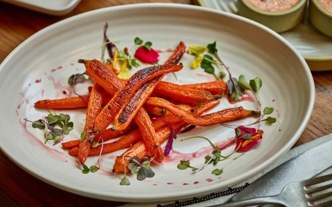 carrots served in a white plate with microgreens and a red sauce 