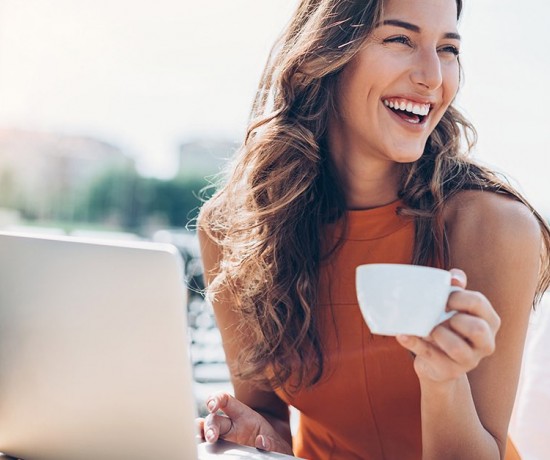 woman sitting at an outdoor table working on her computer and drinking coffee