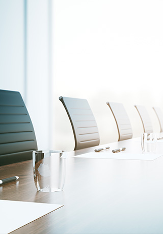 a row of chairs at a conference table with empty glasses, and pens and paper on the table