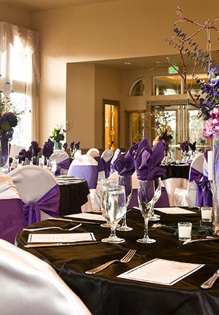 wedding reception tables with white chair covers and purple bows and black tablecloths
