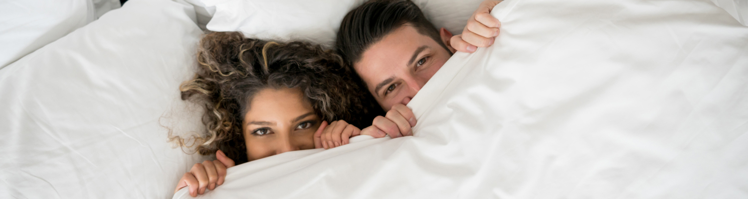 couple covering themselves in them bed with a white blanket