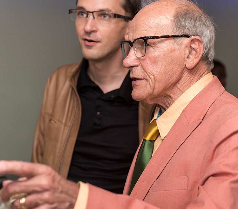 man in coral suit talking to another man in brown leather coat