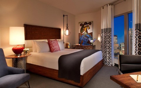 View of a stylish hotel room with features as a queen bed, nightstand and a study desk