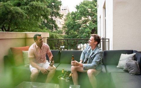 two men drinking a beer on a couch on a balcony