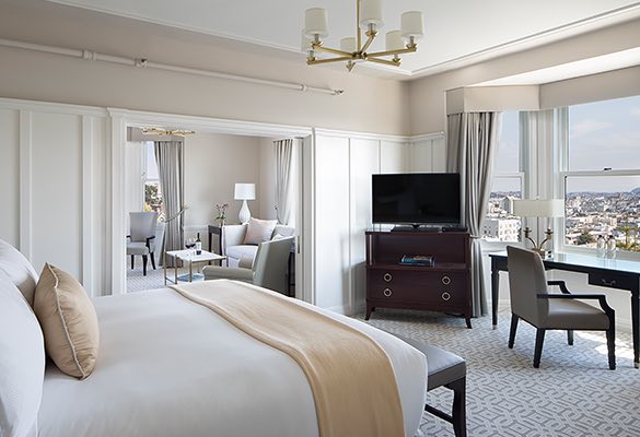 Bed with gold throw, tv in corner, desk with chair in front of window