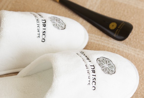 soft white slippers engraved with black hotel drisco logo