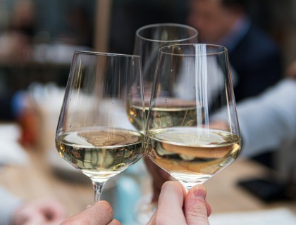 Three glasses of white wine being clinked together at a dinner table.
