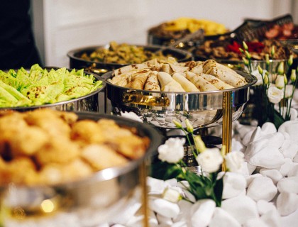 A setup of hot food served in gold trimmed chafing dishes on top of a white linen table.