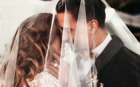 A groom looking at his bride with her veil covering both of their faces.