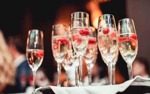Multiple glasses of champagne with raspberries on a white linen tray.