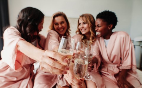 Four women smiling and clinking their champagne glasses in a room with natural light.