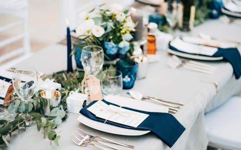 A table setup for dinner with white and navy linen, candles, and floral centerpieces.