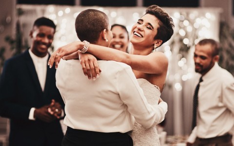 A bride and a groom dancing with guests watching and smiling in the background.
