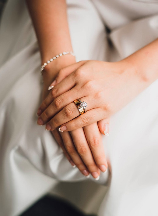 A bride wearing her gold wedding set with her hands crossed on her lap.
