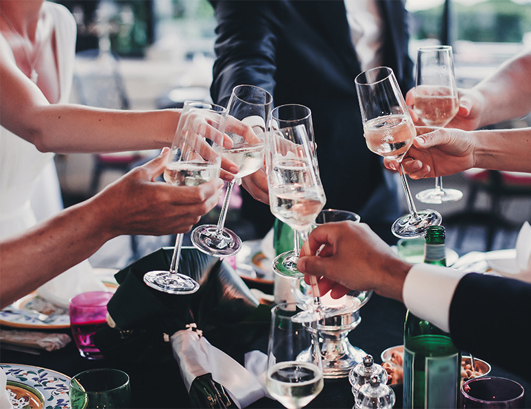 A group of wedding guests clinking their champagne glasses while standing.