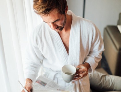 a man in a white robe drinking a coffee reading a magazine
