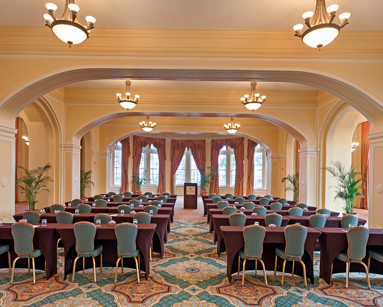 A room set up for an auditorium style meeting with rows of tables and chairs and a podium at the front