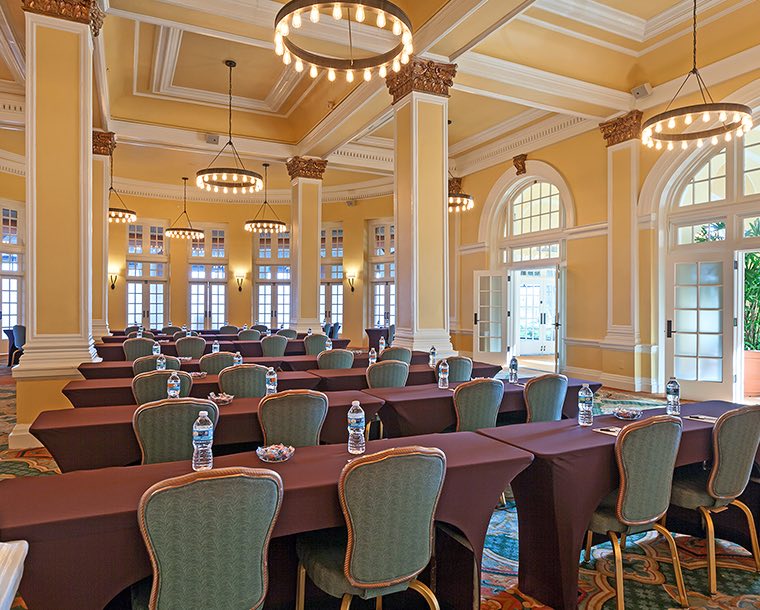 Angled view of rows of tables in a room with tall ceilings and lots of windows