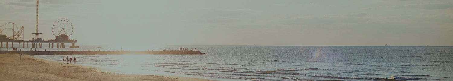 wide view of water from beach with the sun and a pier carnival in the background