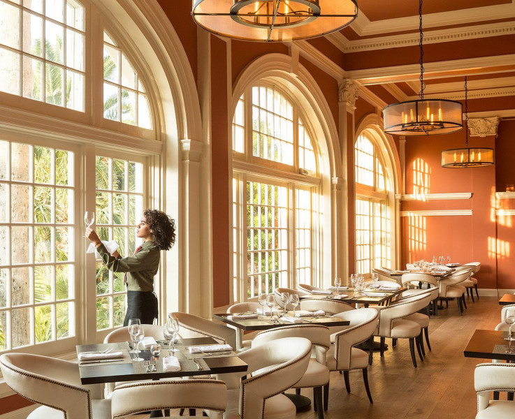 A waitress holds a wine glass towards the window to check for clarity in an empty dining area